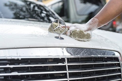A man cleans the hood of a white Mercedes-Benz in Car Services | Quality Import Services